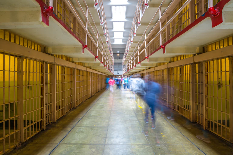 A hall of prison cells with blurred people moving throughout