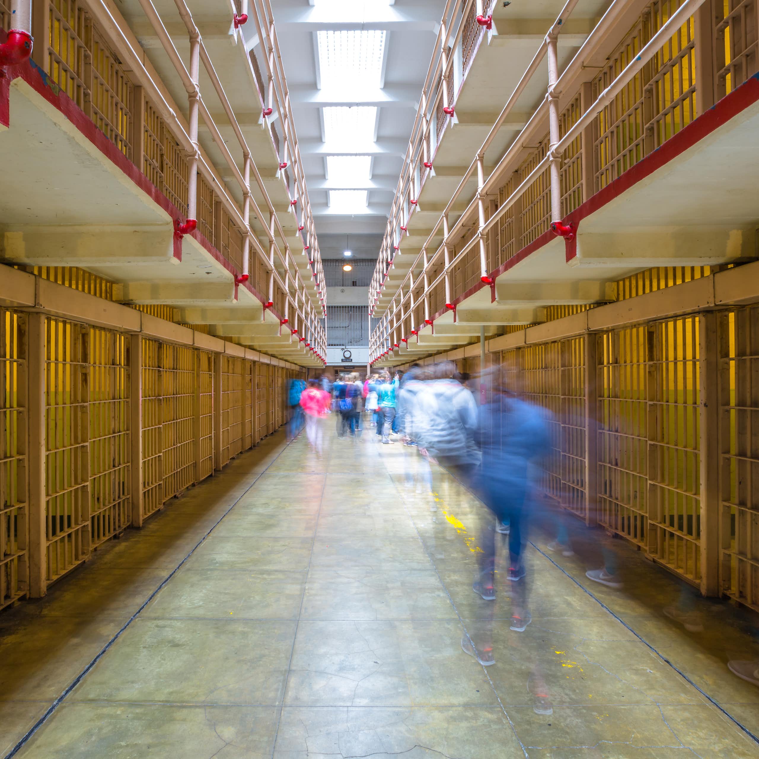 A hall of prison cells with blurred people moving throughout