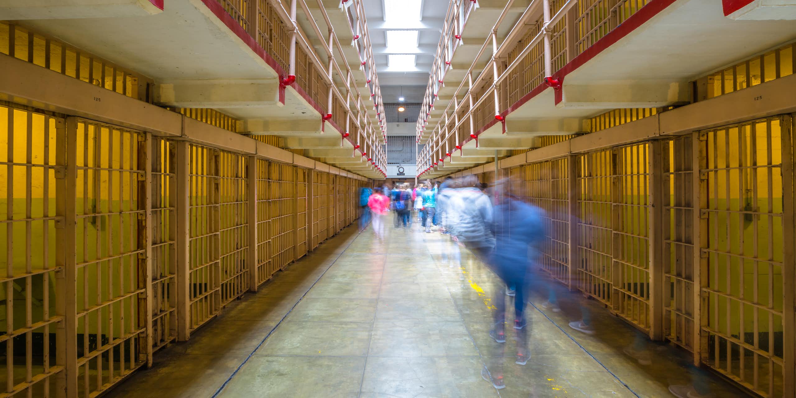 A hall of prison cells with blurred people moving throughout