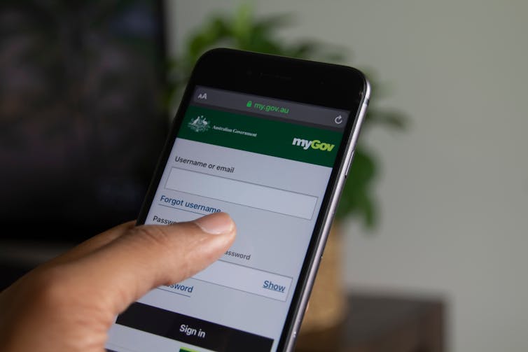 A hand holding a smart phone with the MyGov website on the screen