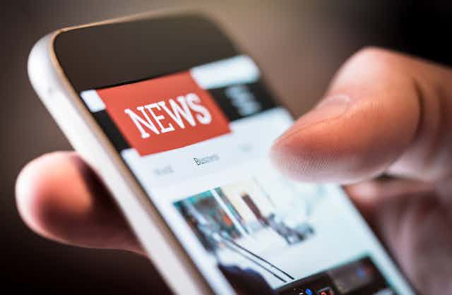 Close-up of a hand holding a smartphone showing a news website.