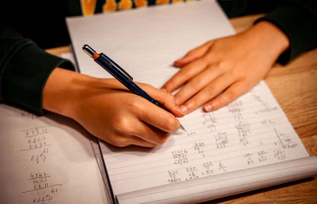 Mãos de uma criança são mostradas fazendo um dever de casa de matemática