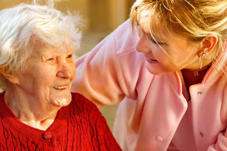 A carer in pink with an elderly lady in red.