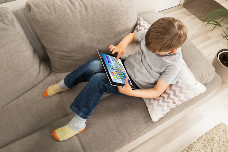 Enfant assis sur un canapé en train de jouer sur une tablette numérique