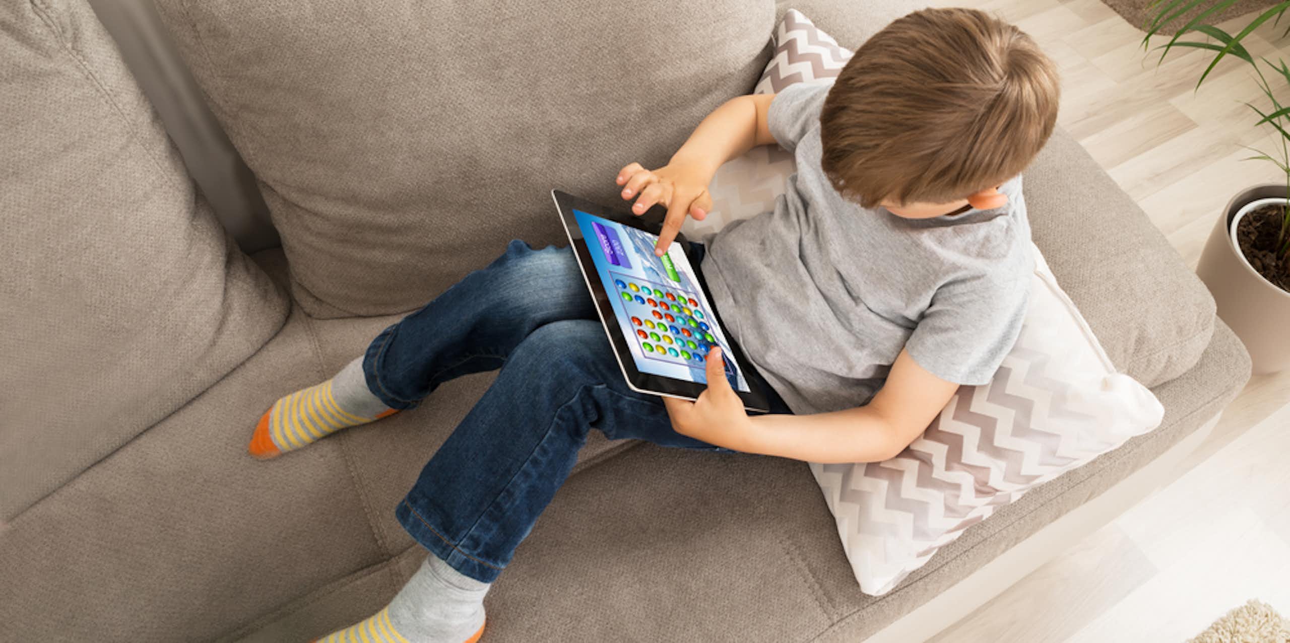 Enfant assis sur un canapé en train de jouer sur une tablette numérique