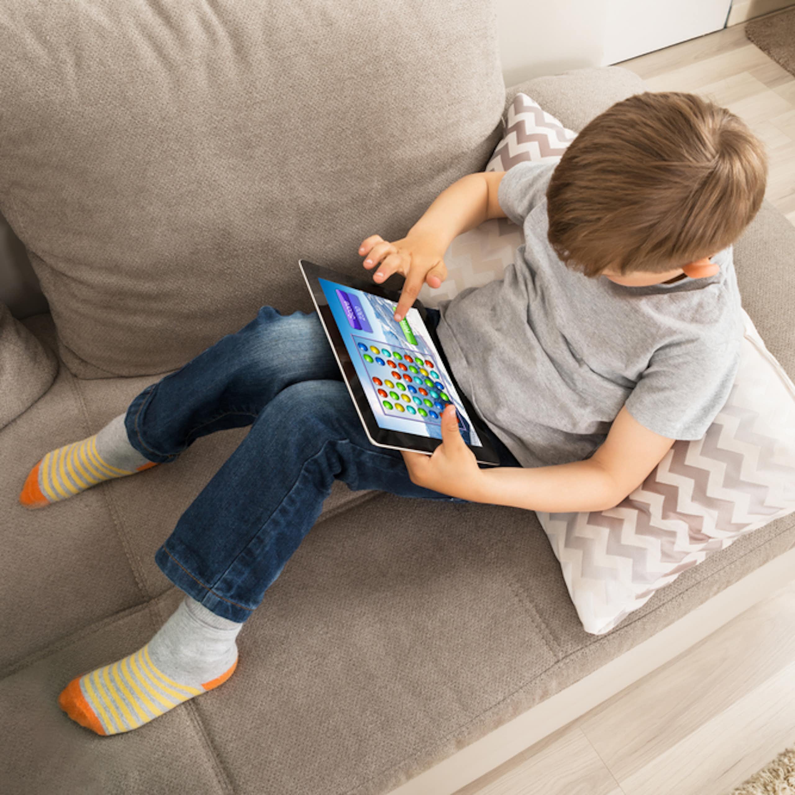 Enfant assis sur un canapé en train de jouer sur une tablette numérique