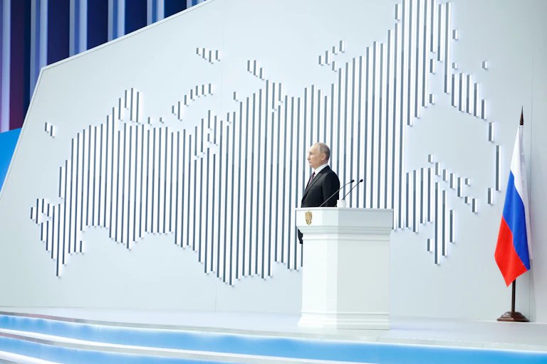 Vladimir Putin stands on a stage in front of a map of the Russian landmass