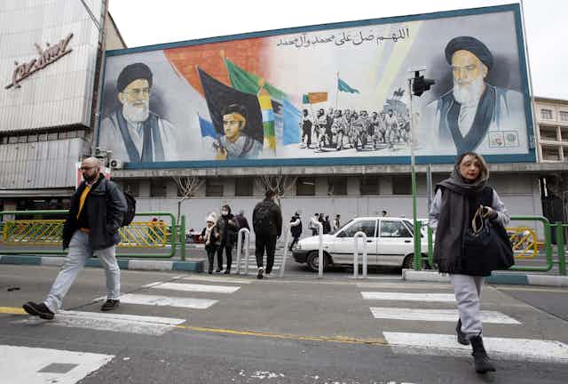 Iranians walk past a large election poster in Tehran.