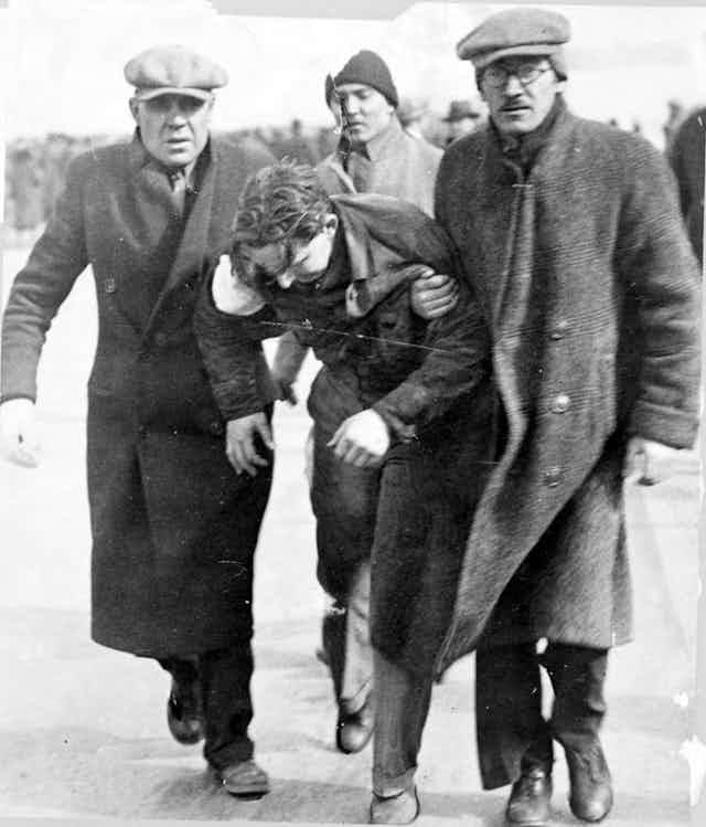 Two men  in winter coats carry a third man who has been injured.