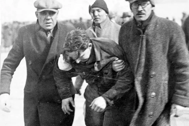 Two men in winter coats carry a third man who has been injured.