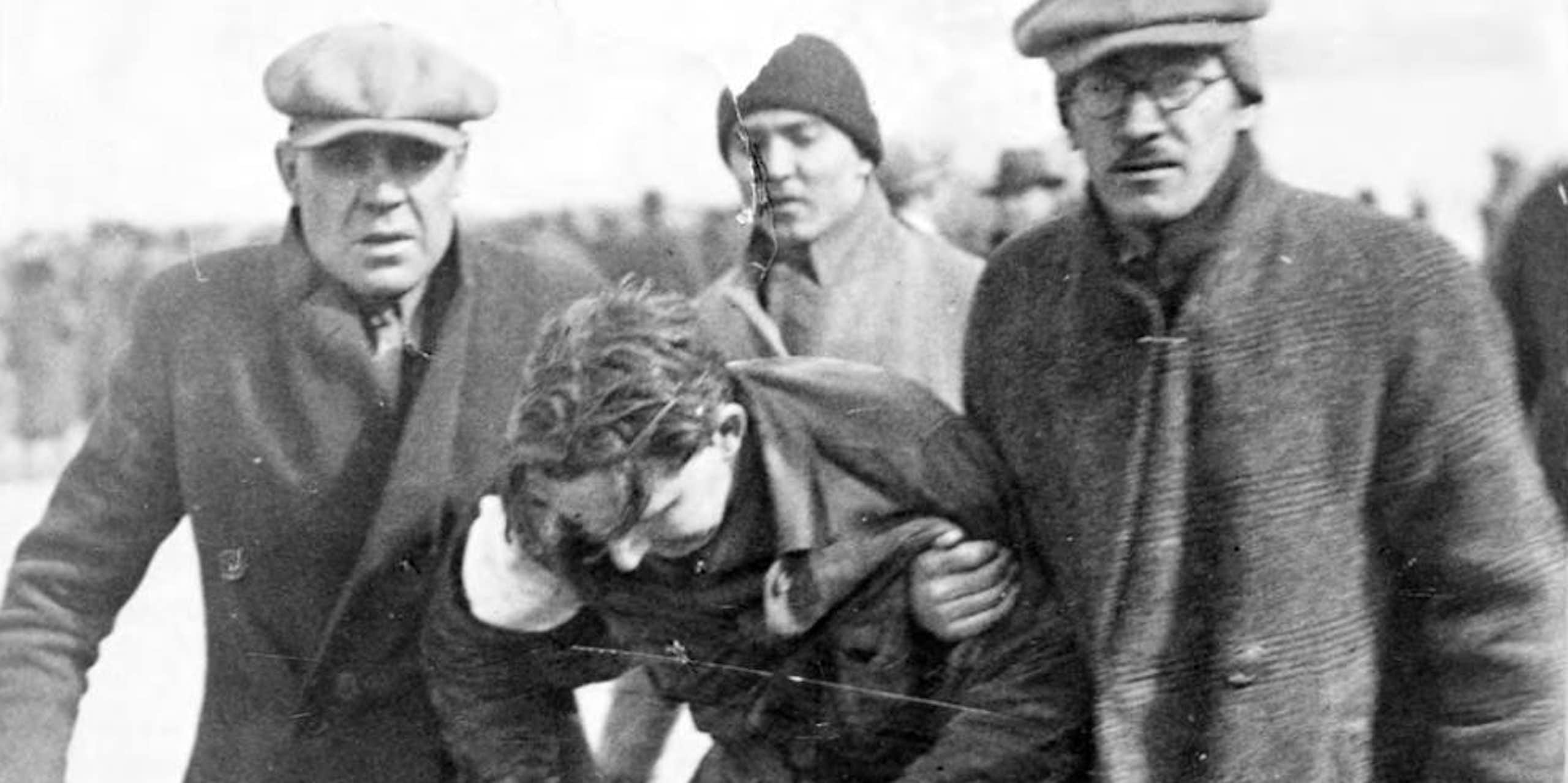 Two men  in winter coats carry a third man who has been injured.