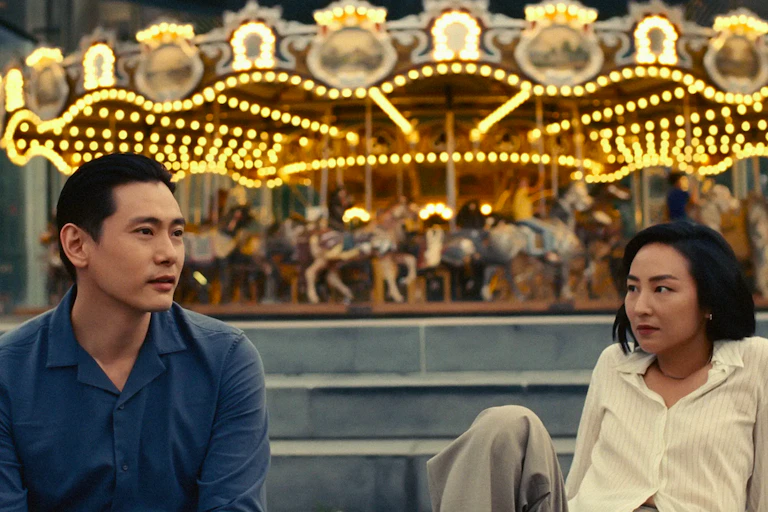 Young Korean man sits near a young Korean woman with a carousel in the background.
