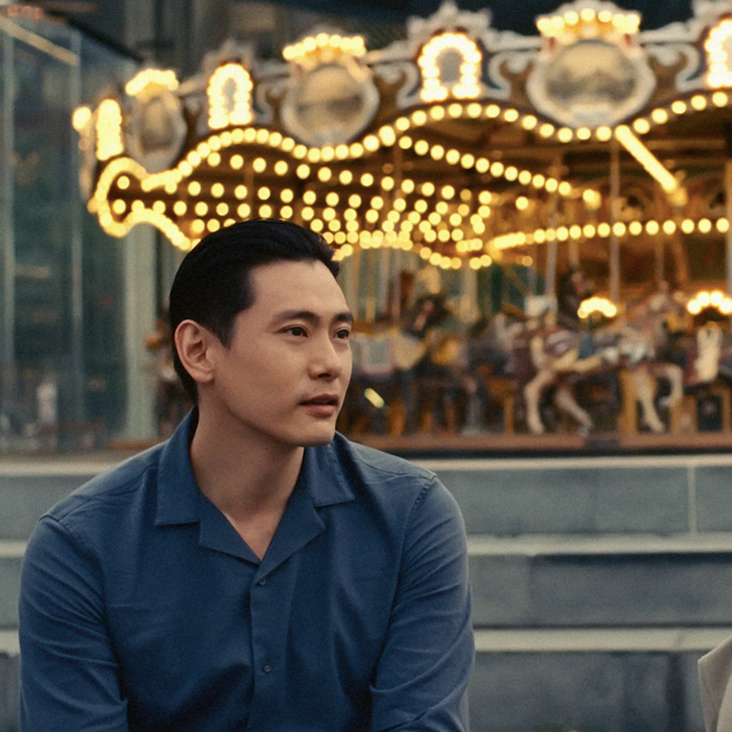 Young Korean man sits near a young Korean woman with a carousel in the background.