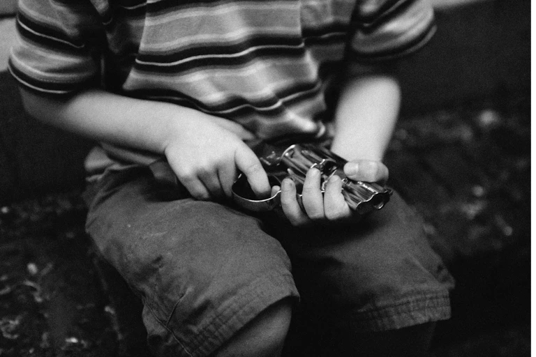 A boy in a striped shirt and shorts holds a revolver. His face is not shown.