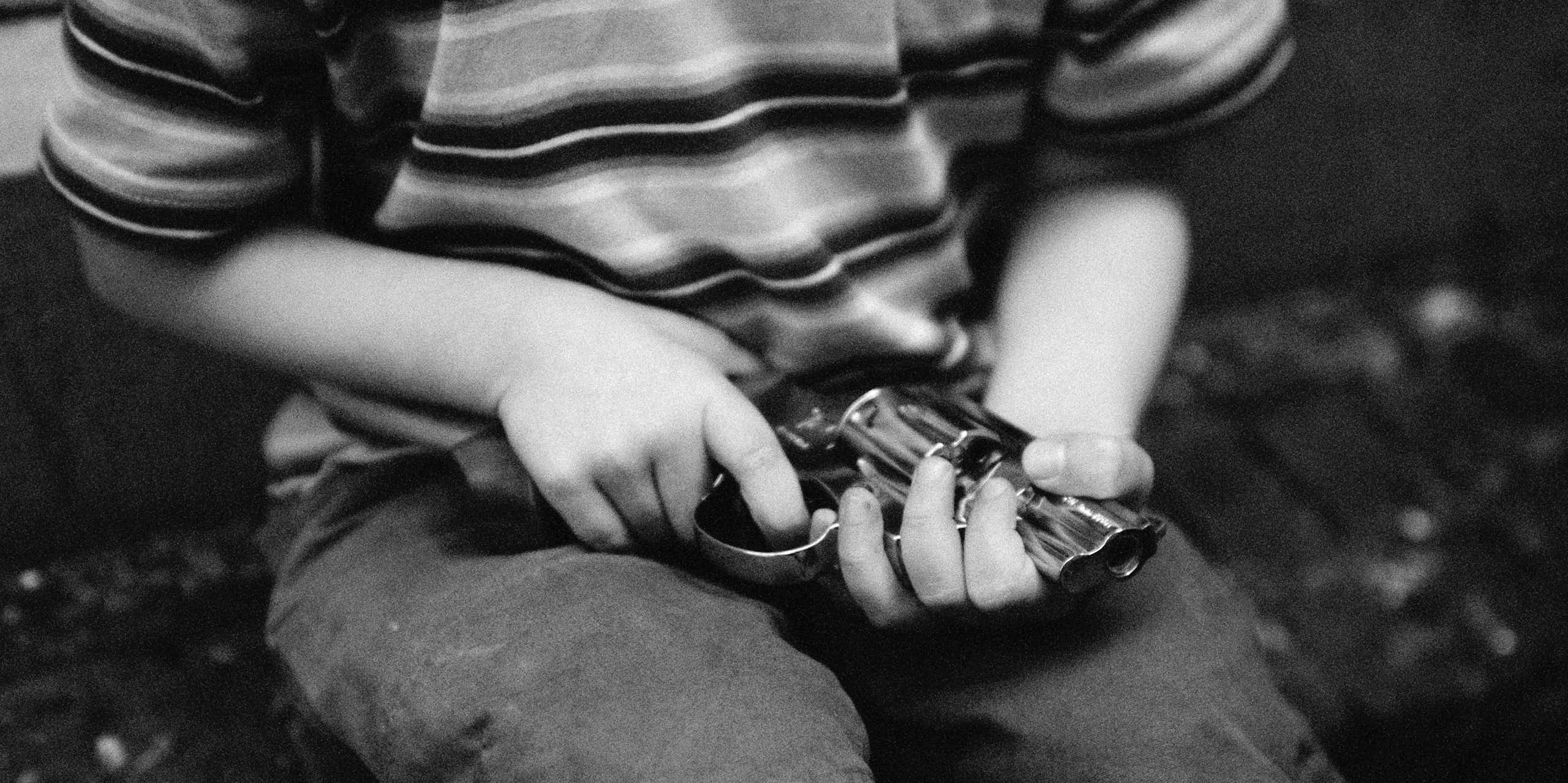 A boy in a striped shirt and shorts holds a revolver. His face is not shown.