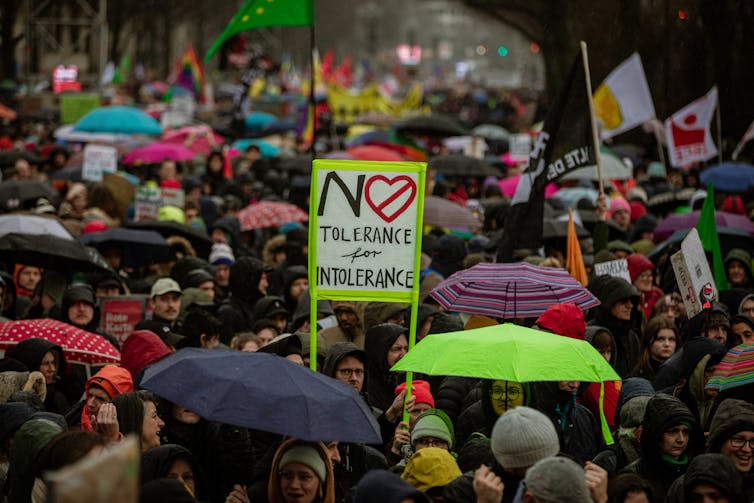 Una gran multitud de personas están muy juntas con paraguas y carteles.  Uno de ellos dice: 