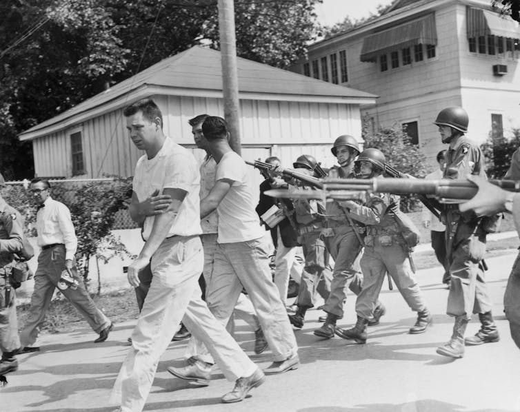 Soldiers with bayonets prod white men from a mob to leave the area.