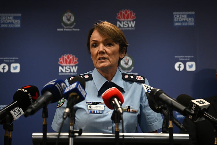 A police woman stands at a lectern covered in media microphones
