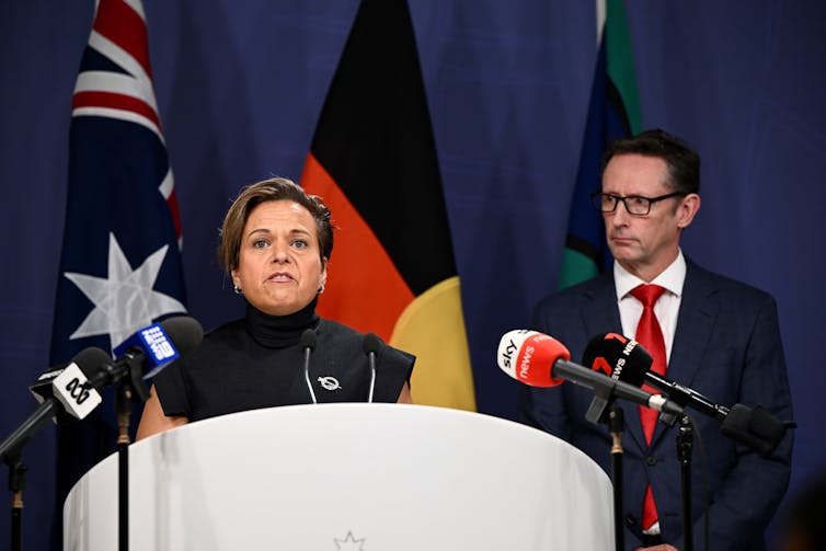 A woman stands behind a lectern and speaks to the media.