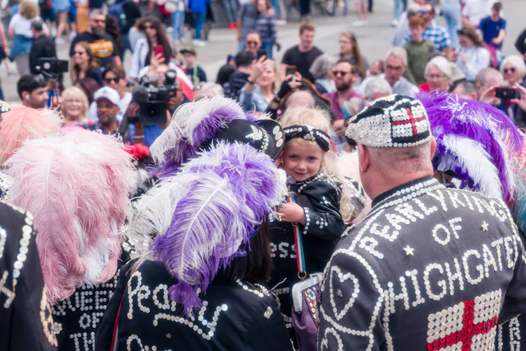 People wearing suits covered in pearly buttons and flamboyant feathers.