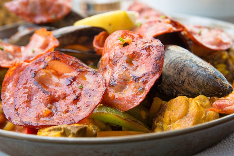 A plate of food with cooked fish and slices of pork or chorizo.
