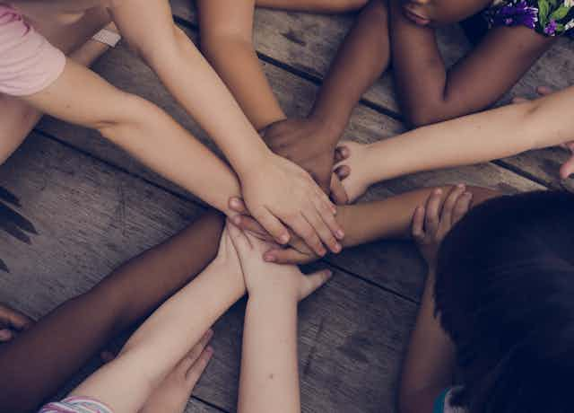 Shot of bare arms, hands all piled on top of eachther, mixed skin tones, wooden background