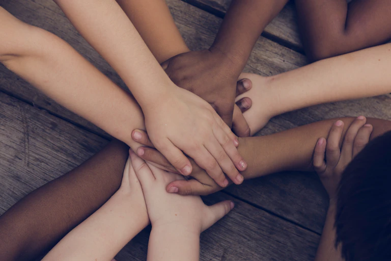 Shot of bare arms, hands all piled on top of eachther, mixed skin tones, wooden background