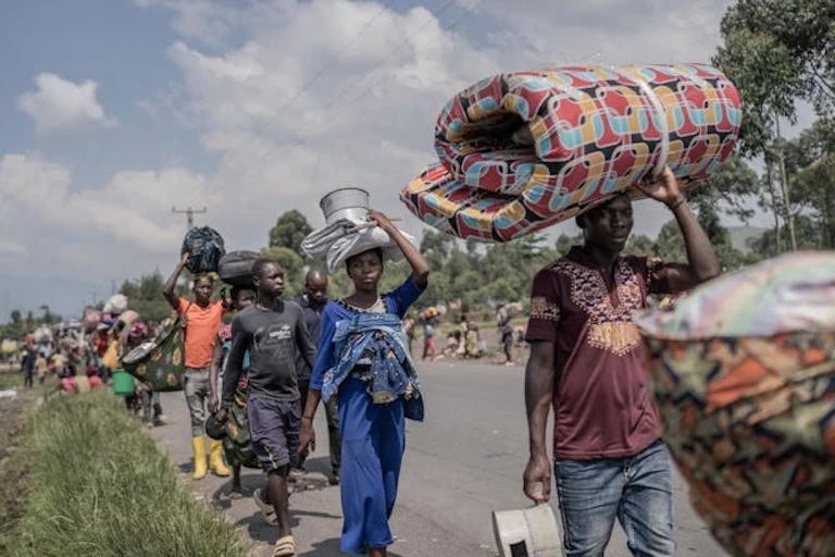 A file of people carrying personal possessions on a rural track