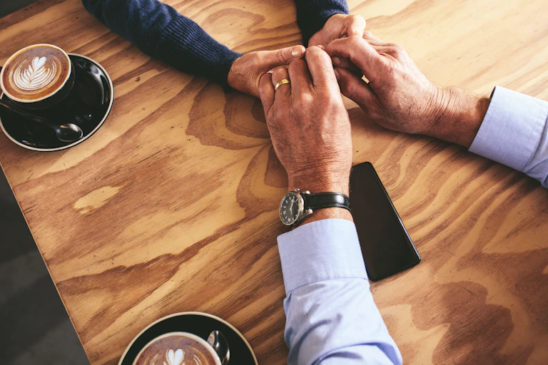 People holding hands over a wooden table, with cups of coffee on the side