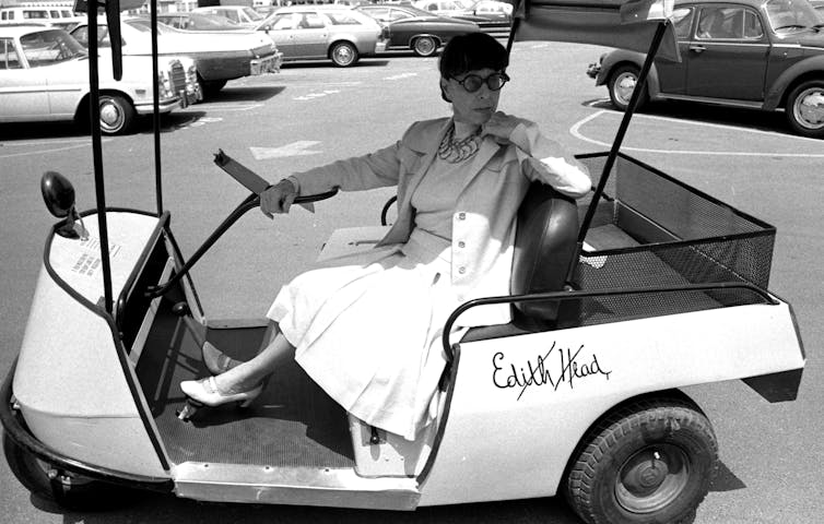 Elderly woman wearing sunglasses poses while sitting in a golf cart.