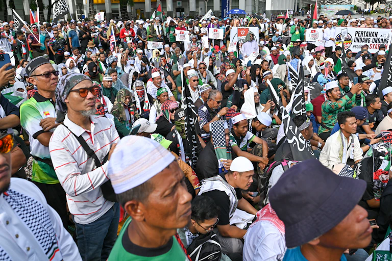 A group of protestors many in Islamic headware stand and sit.