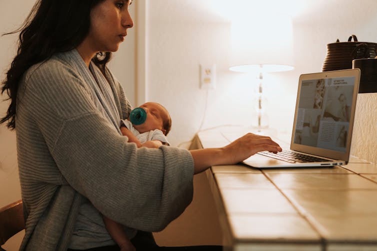 Woman using laptop carries a baby.