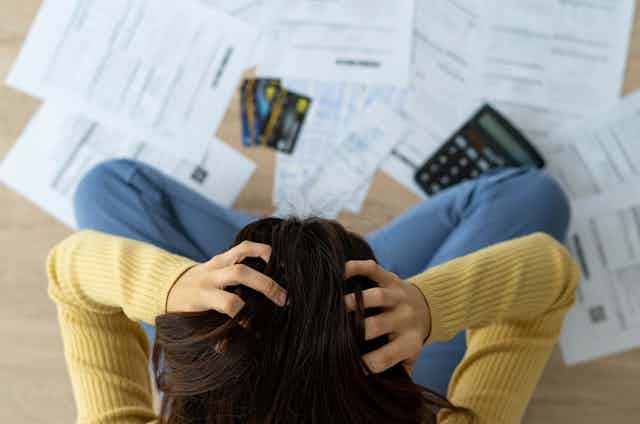 Top-down view of a woman sitting in front of a pile of paperwork with her head in her hands