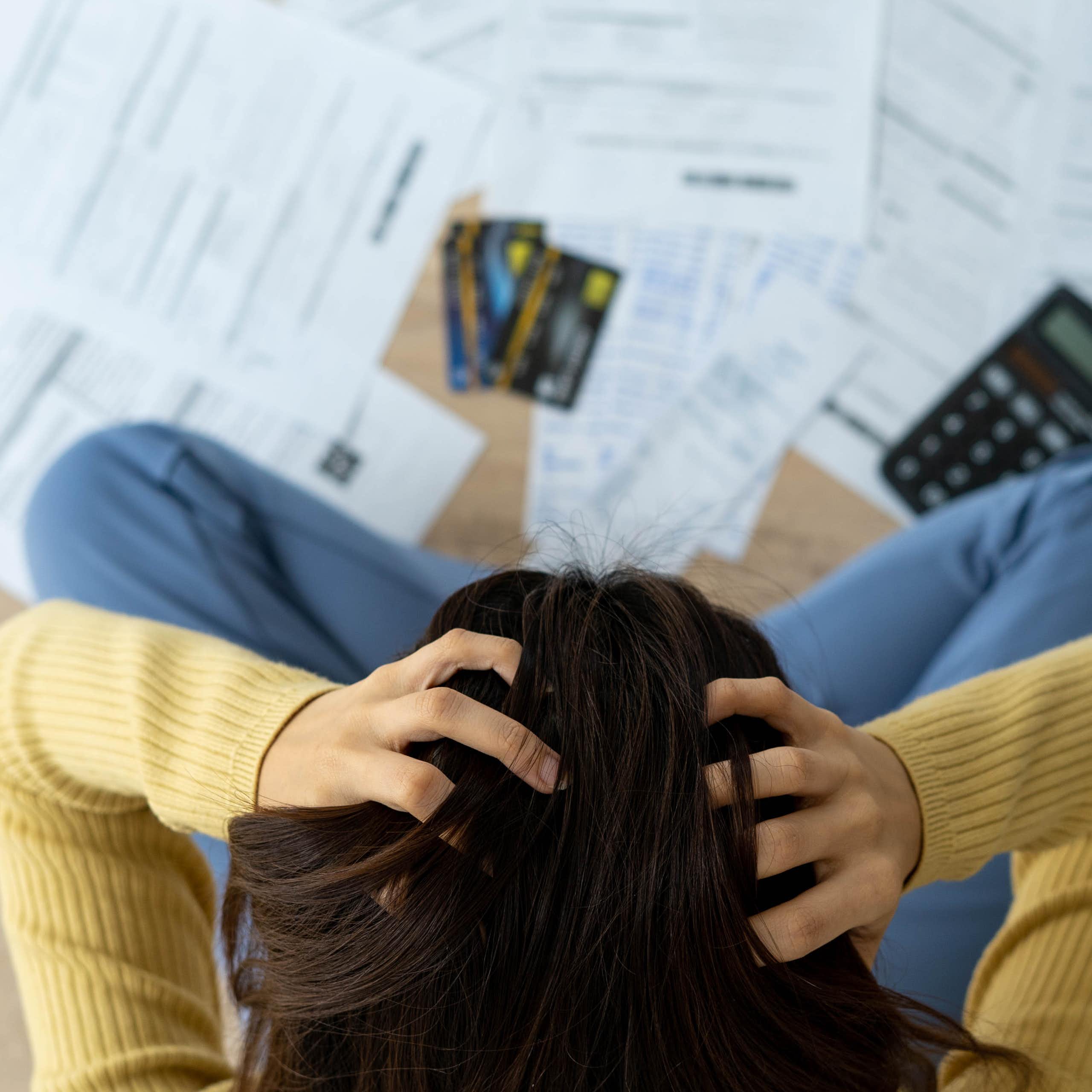 Top-down view of a woman sitting in front of a pile of paperwork with her head in her hands