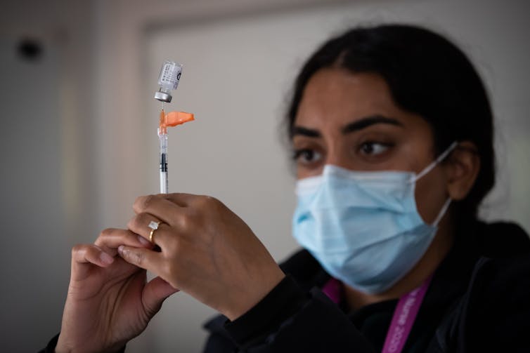 A woman in a face mask fills a medical syringe up from a vial