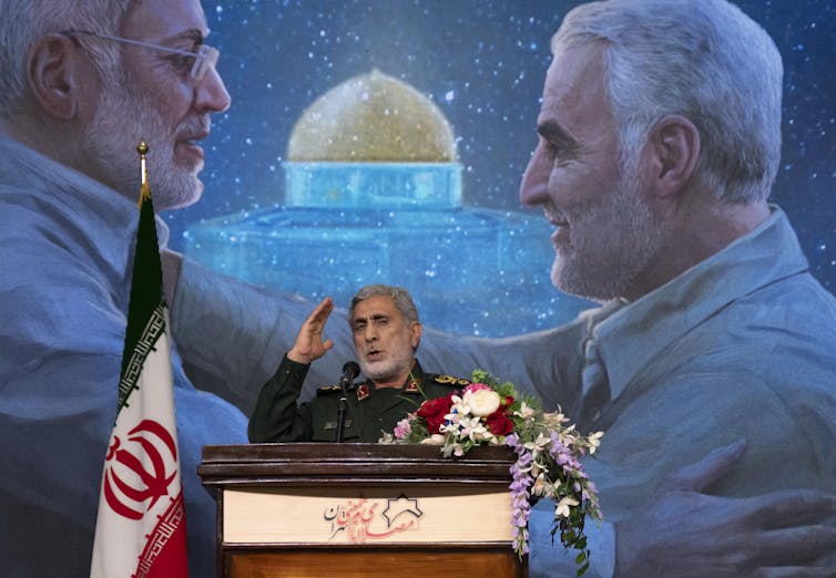 Man speaking in front of image of two men.