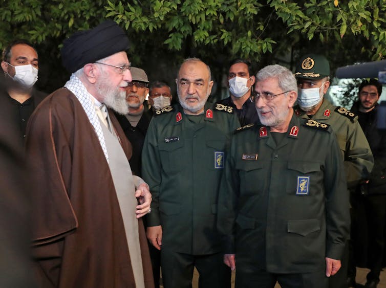 Three Iranian leaders, two in military fatigues stand and talk.
