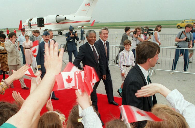 Mandela and Mulroney walking on red carpet with plane in background