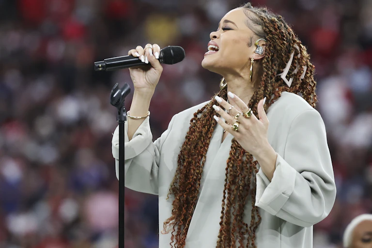 A Black woman with long hair is holding a microphone while singing a song