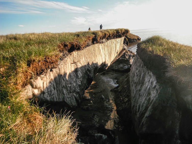 Two people stand on a cliff with permafrost evident.