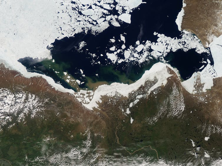 A satellite view of the Arctic coast showing a river and sea ice breaking up.