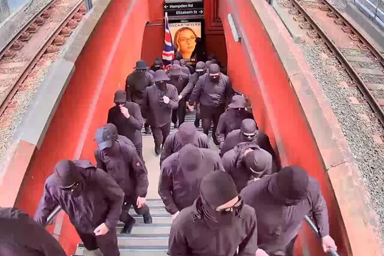 A group of people in black clothes and balaclavas at the train station.
