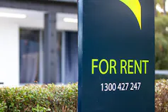 A board advertising that a property is available for rent outside a suburban home