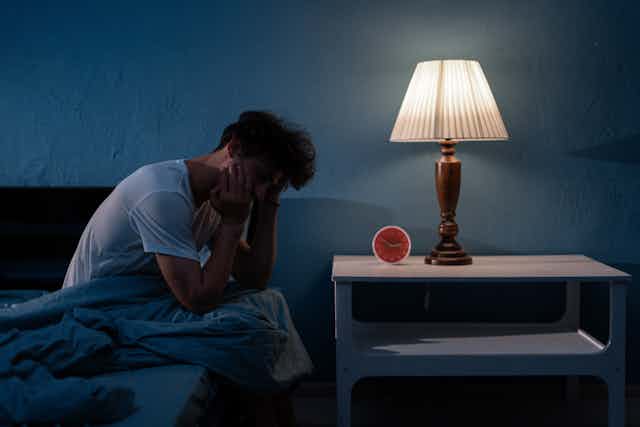 A man sitting on the edge of his bed at night.