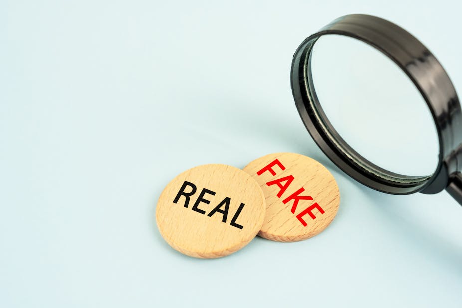 An illustration of a magnifying glass poised over two wooden discs. Fake is written on one; real on the other