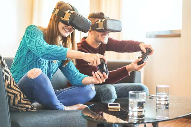 Una pareja de jóvenes jugando a videojuegos con mandos y gafas de realidad virtual.