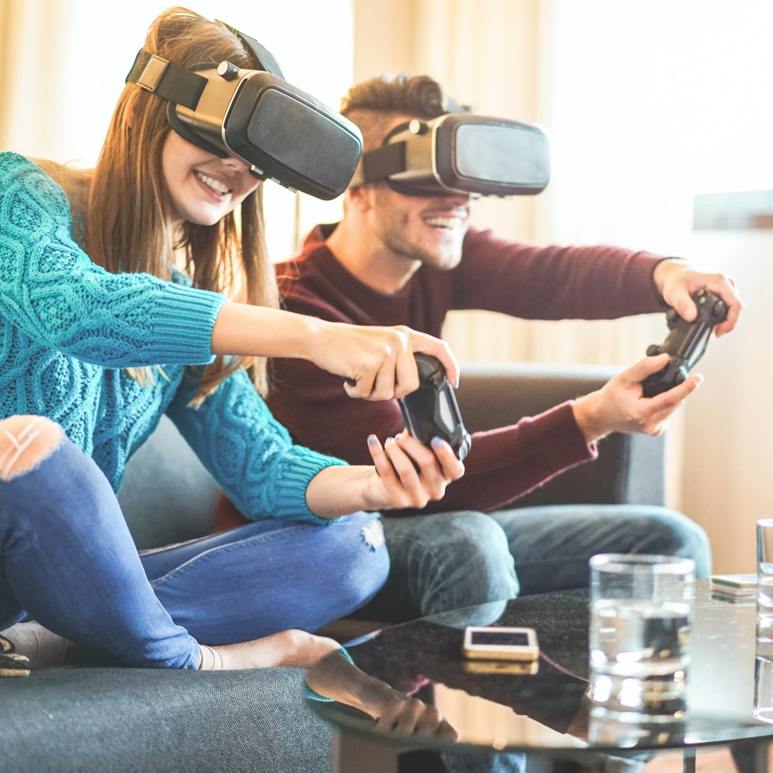 Una pareja de jóvenes jugando a videojuegos con mandos y gafas de realidad virtual.