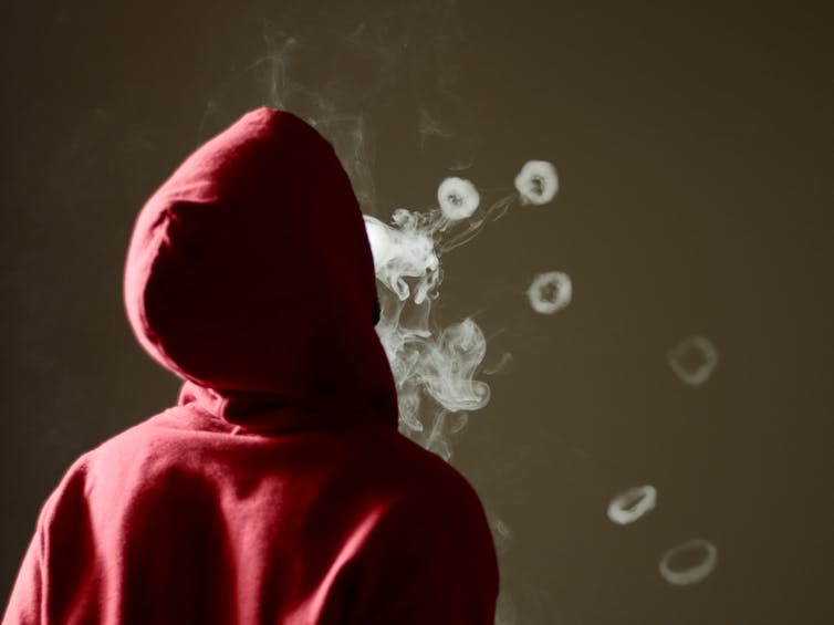 Person in hoodie seen from behind blowing smoke rings