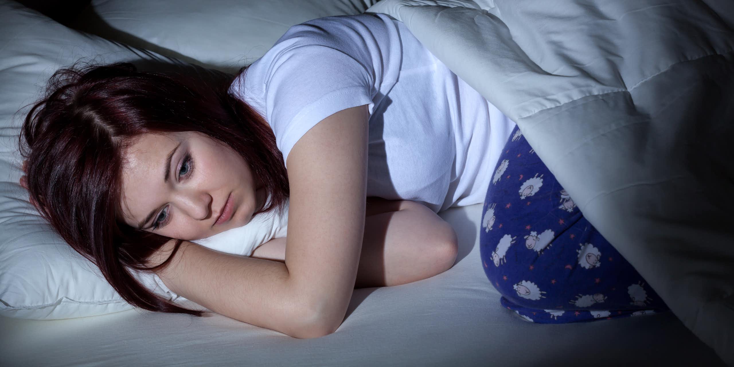Une jeune femme est allongée dans son lit et semble peiner à trouver le sommeil.