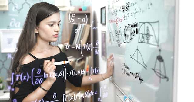 Jeune fille face à des équations de maths sur un tableau blanc dans une salle de classe